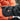 Black heated glove with visible brand logo, worn by a person in an orange jacket.