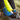 A close-up outdoor shot of a person sitting on the ground, wearing a bright blue and navy striped hiking sock while trying on brown hiking boots. The person is also wearing a bright yellow puffer jacket and black pants.
